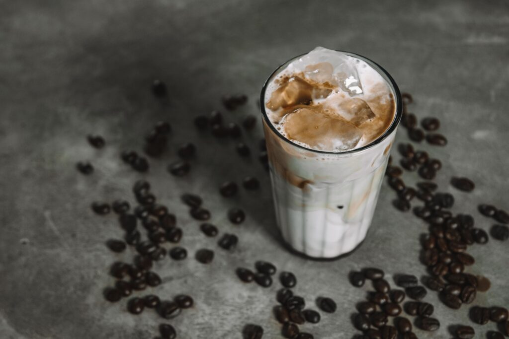 Refreshing iced coffee with milk and ice cubes surrounded by coffee beans on a rustic surface.